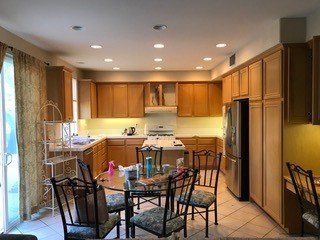 Spacious kitchen with wooden cabinets, tiled floor, and a round glass dining table with chairs.
