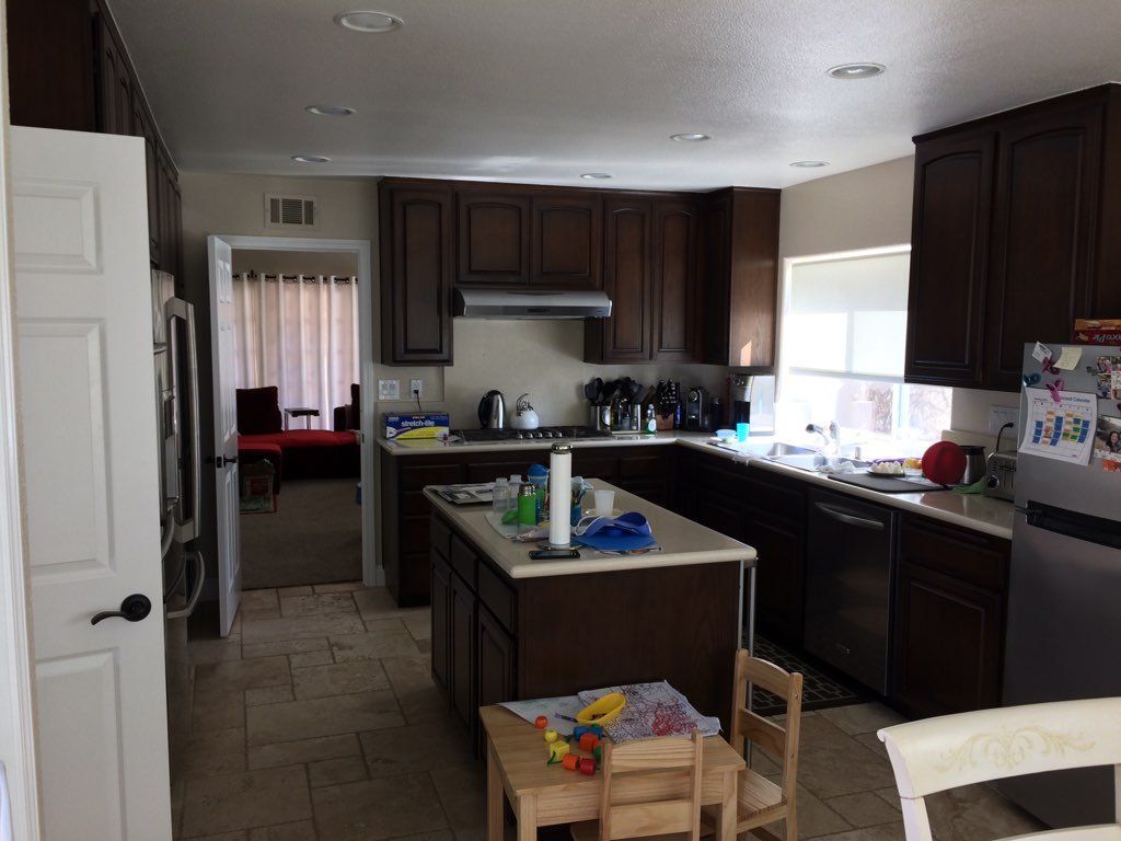 Kitchen interior with dark wood cabinets, island, and countertop clutter near a bright window