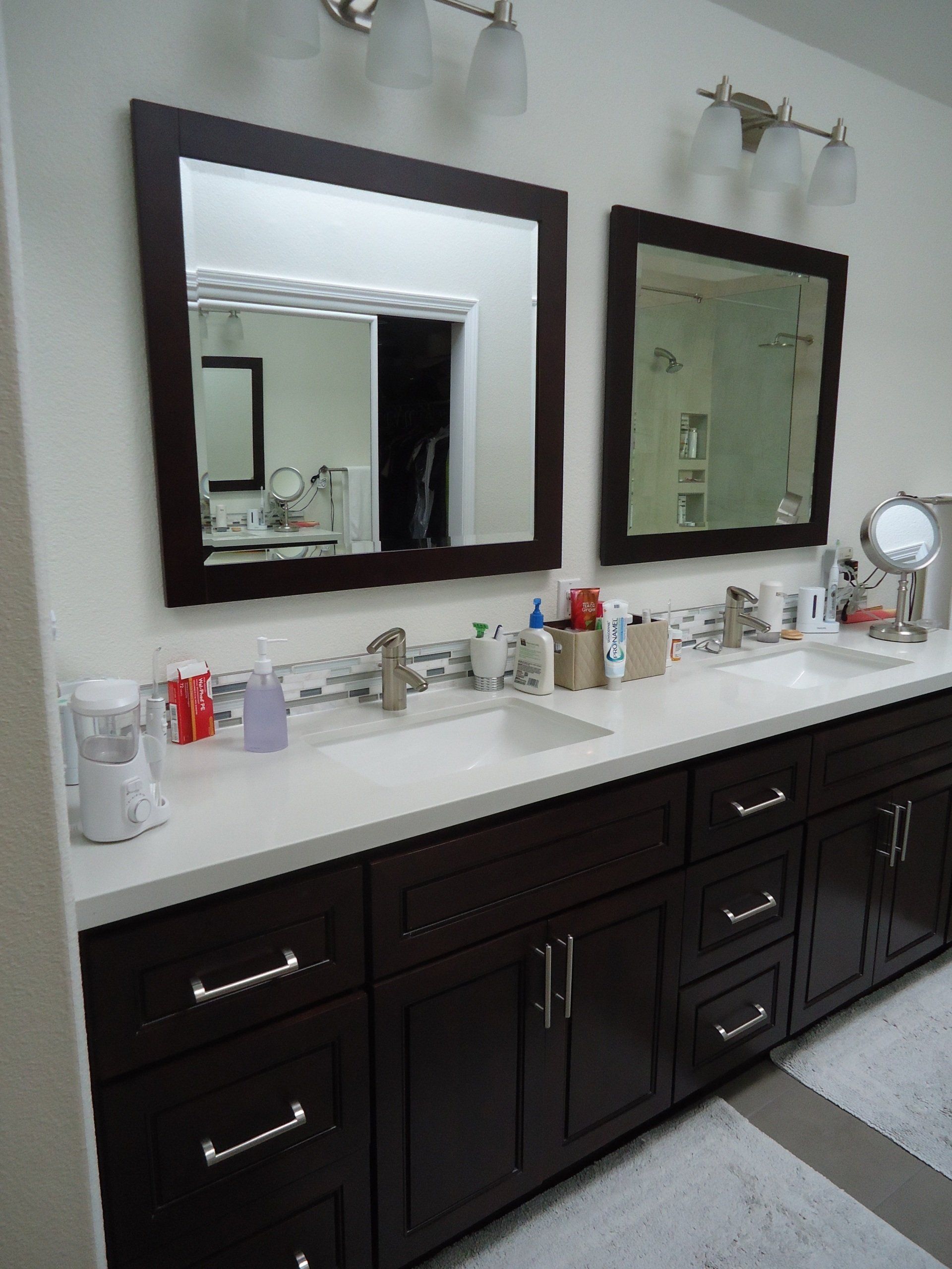 Bathroom vanity with two mirrors, white countertop, dark cabinets, and toiletries arranged on top