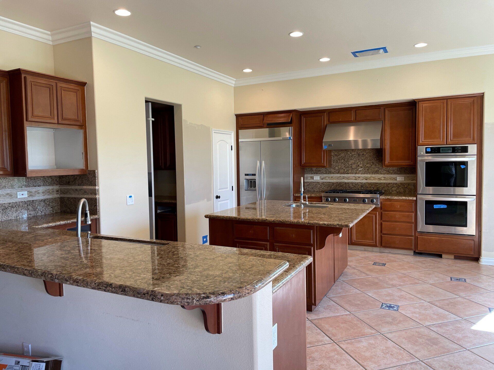 Modern kitchen with granite island, wood cabinets, stainless appliances, and beige tile floor