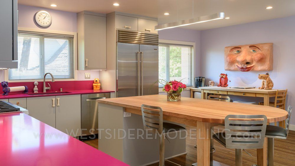 Modern kitchen with bright pink countertops, stainless steel appliances, and a wooden dining table by a wall art portrait