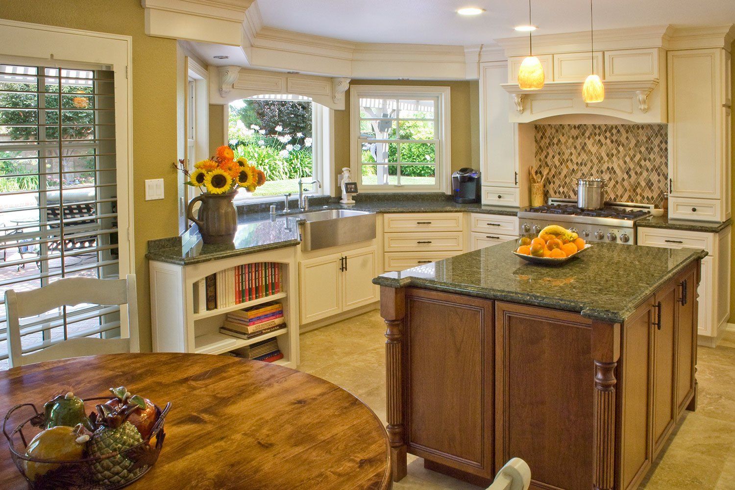 Bright kitchen with granite island, white cabinets, and vase of sunflowers by a window.