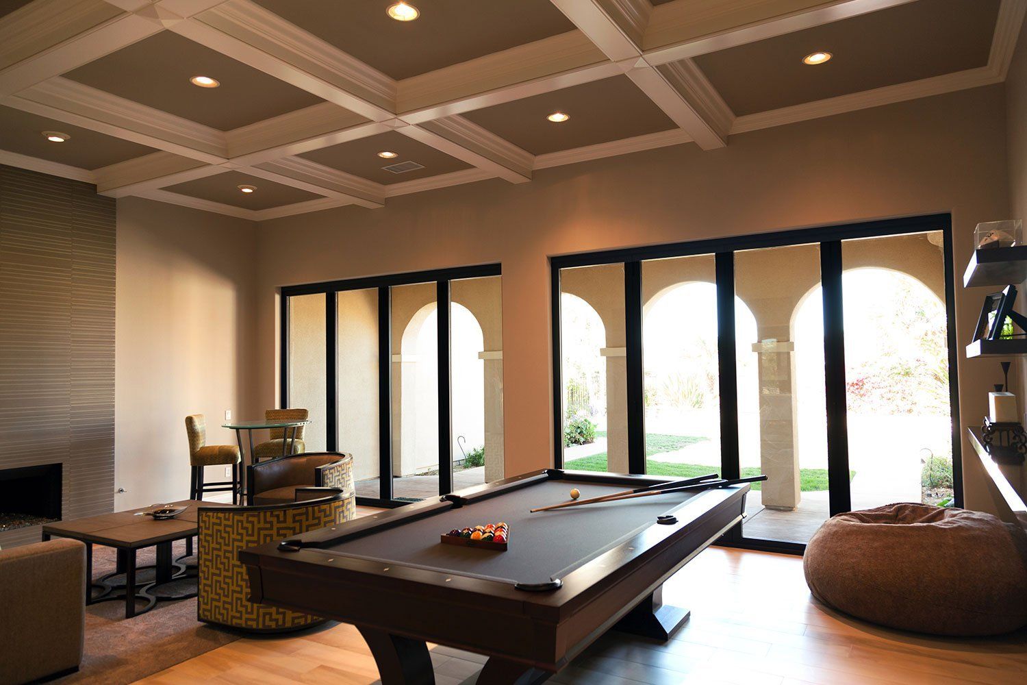 Modern game room with a pool table, lounge seating, and arched glass doors opening to bright outdoors