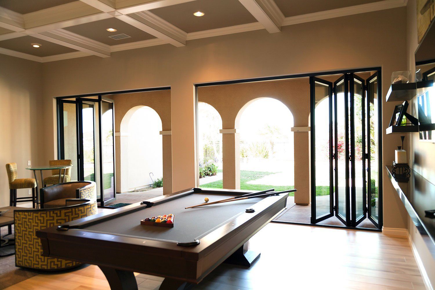 Spacious game room with a pool table, large arched windows, and folding glass doors opening to a patio.