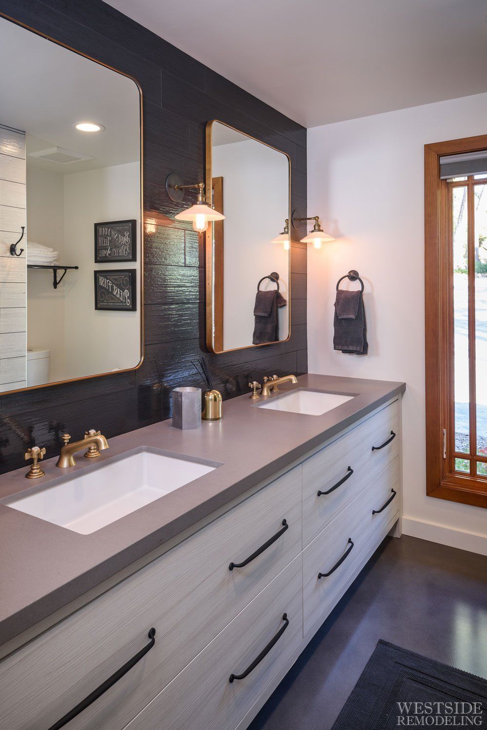 Modern bathroom vanity with double sinks, dark mirror frame, brass fixtures, and a glass shower door
