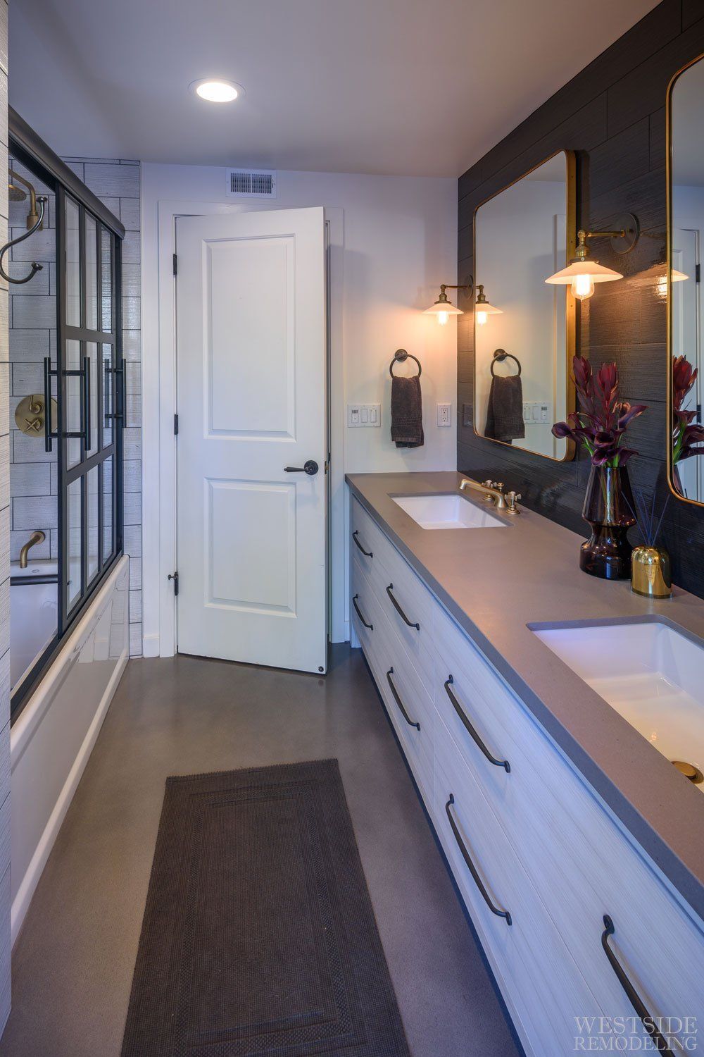 Narrow bathroom with white vanity, large mirror, glass shower, and gray runner rug.