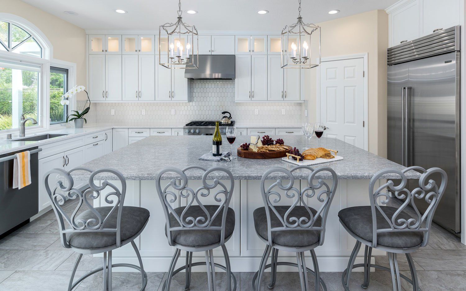 Bright white kitchen with island, barstools, chandelier, and stainless steel appliances