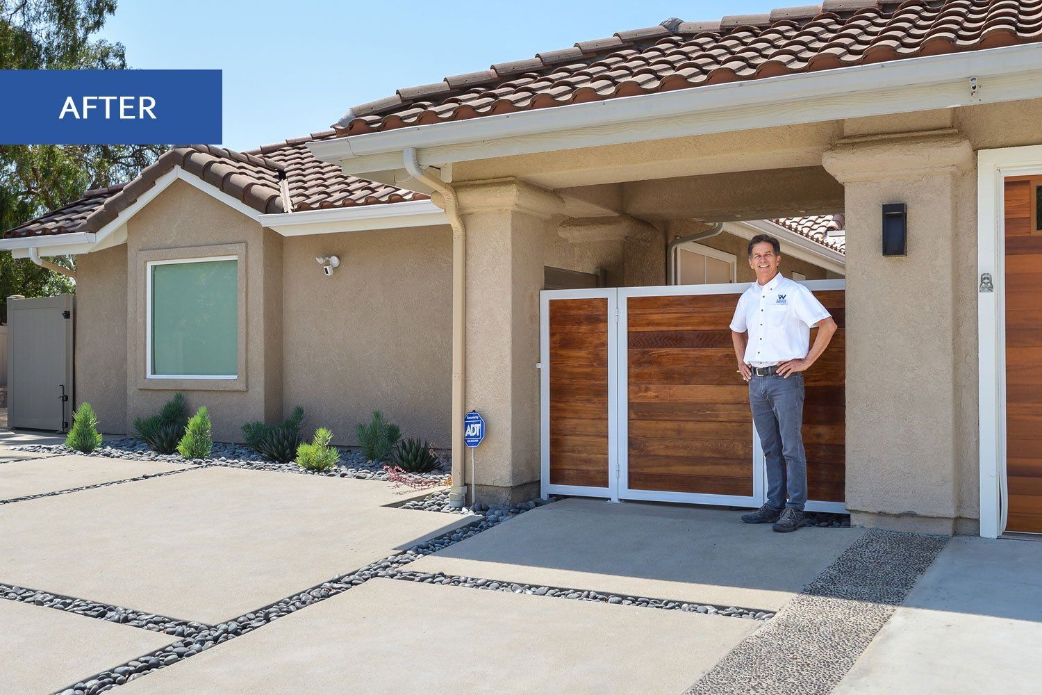 Front exterior of a stucco house with a man standing by a wooden gate under a covered entry.