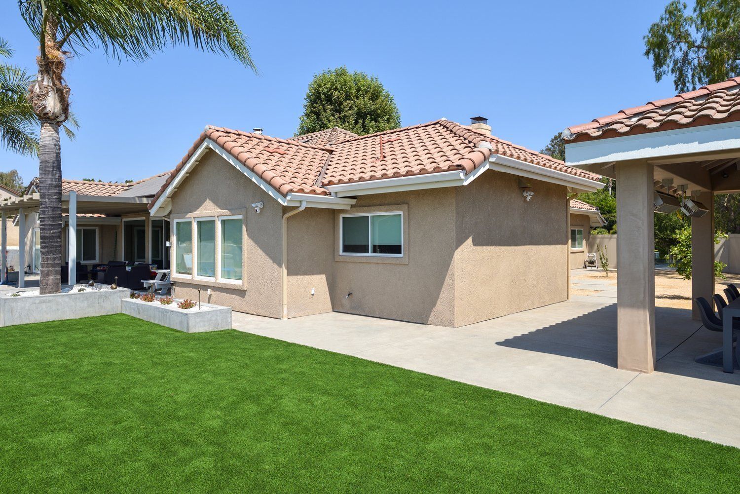 Single-story beige house with red tile roof, green lawn, and covered patio on a sunny day