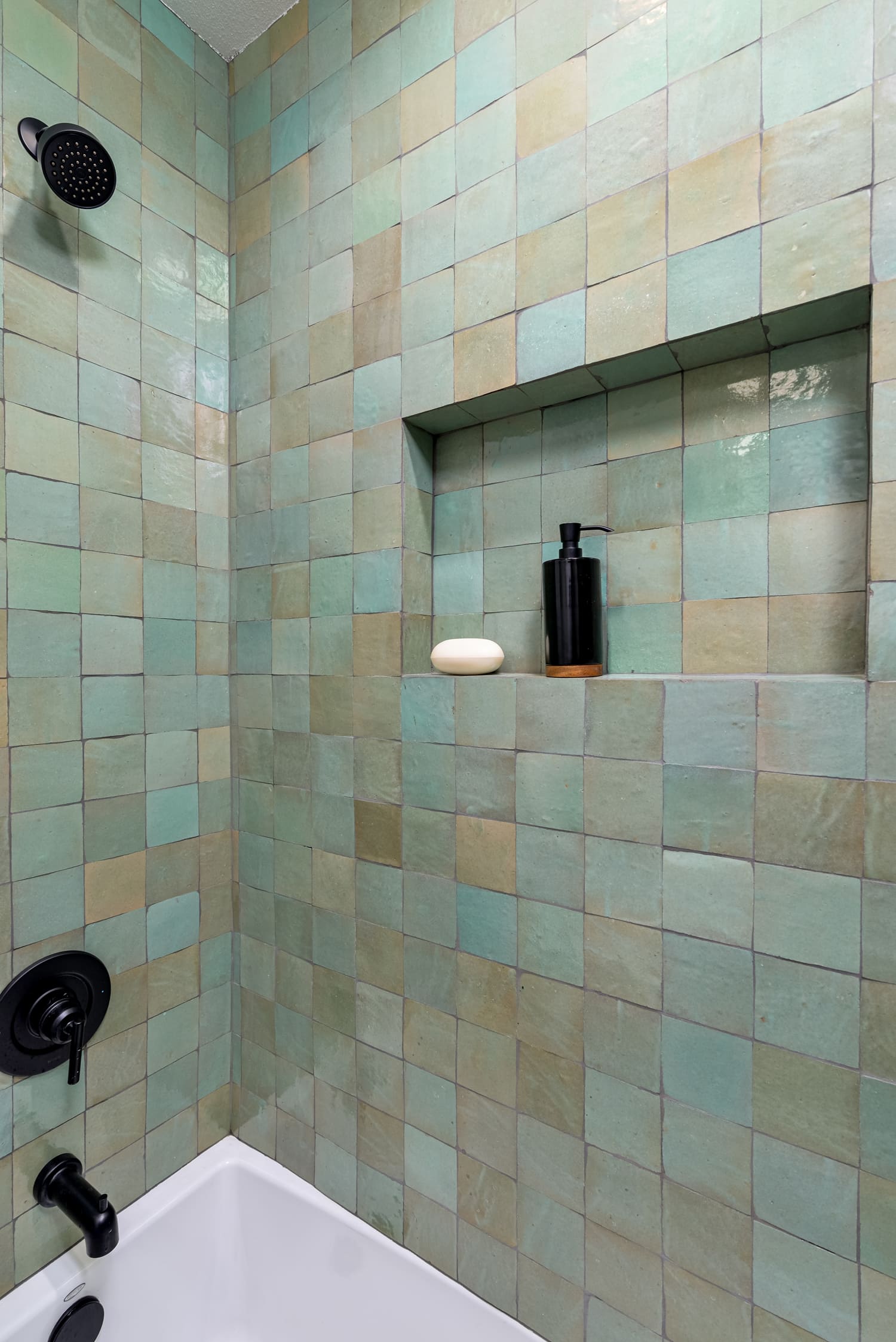 Shower stall with mint-green tile walls, built-in shelf, and black shower fixtures