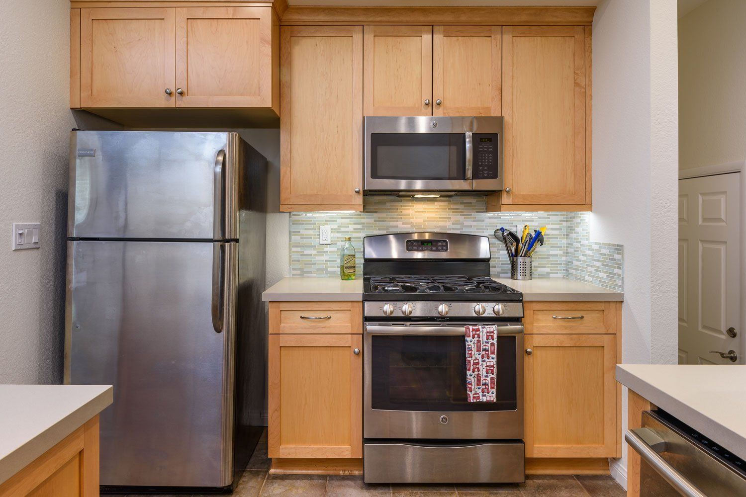 Compact kitchen with stainless steel appliances, wooden cabinets, and light tile backsplash