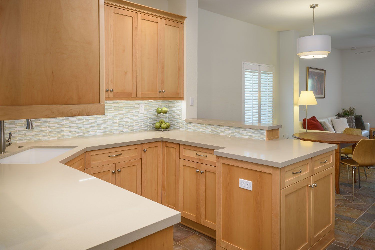 Bright kitchen with light wood cabinets, white countertops, and a dining area in the background