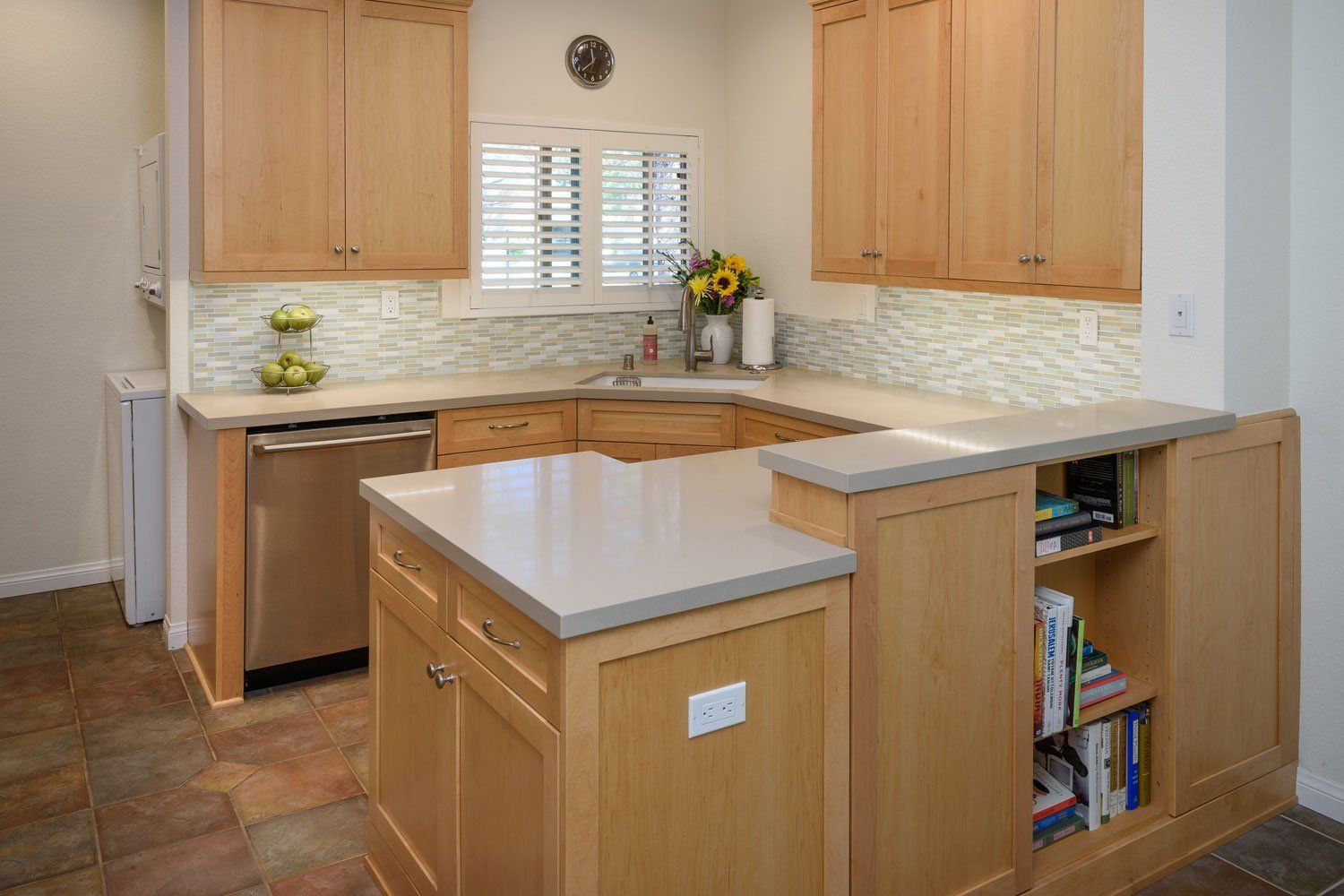 Bright kitchen with light wood cabinets, white countertops, and a small island with open shelves.