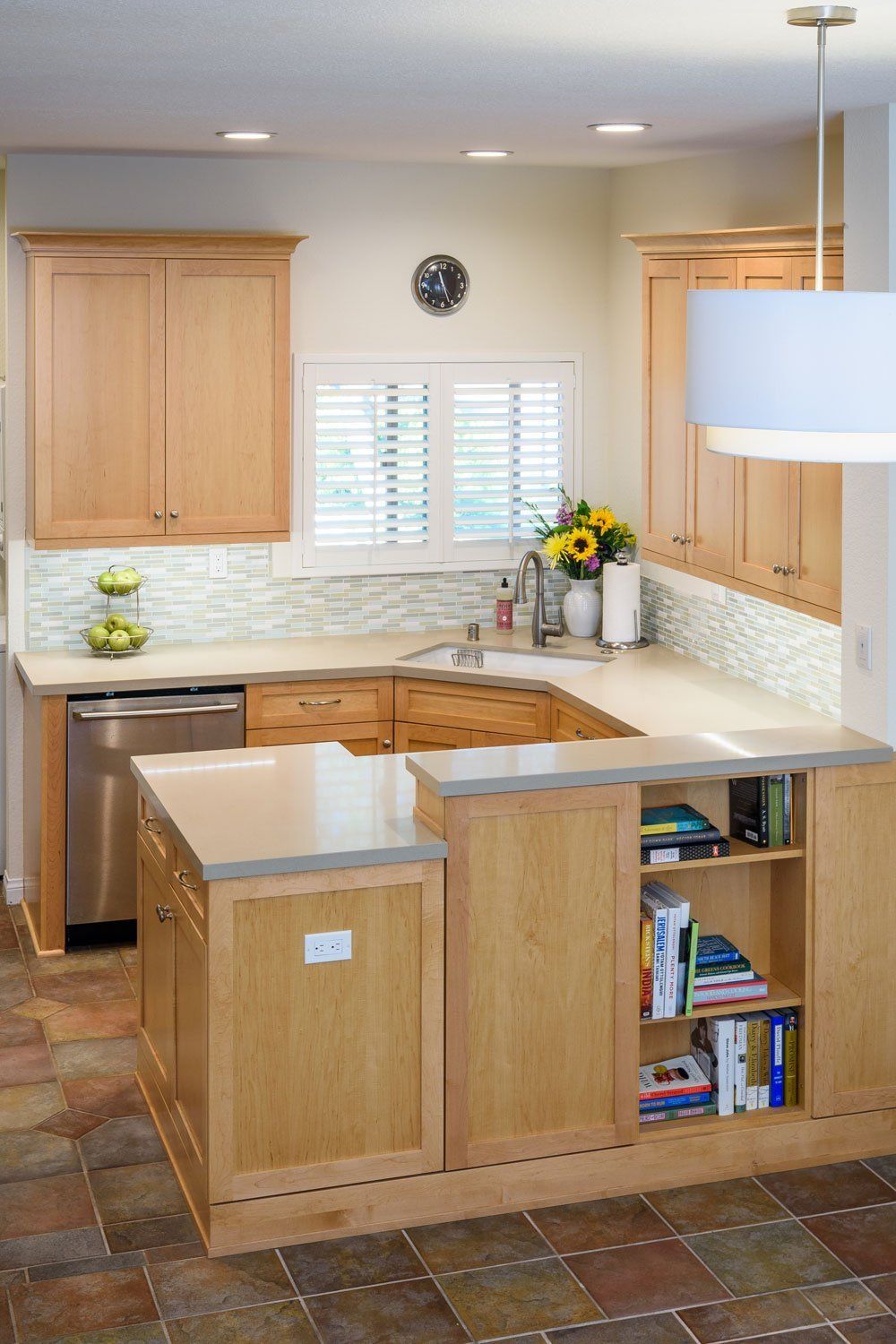 Bright kitchen with light wood cabinets, island, tile floor, and white countertops by a window
