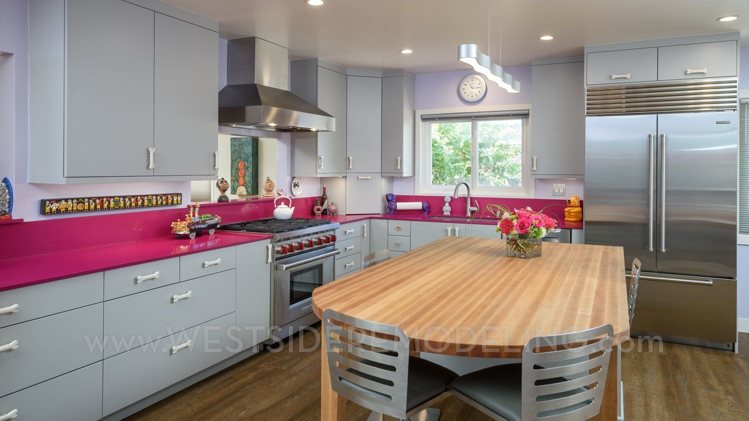 Modern kitchen with gray cabinets, pink backsplash, wooden island table, and stainless steel appliances