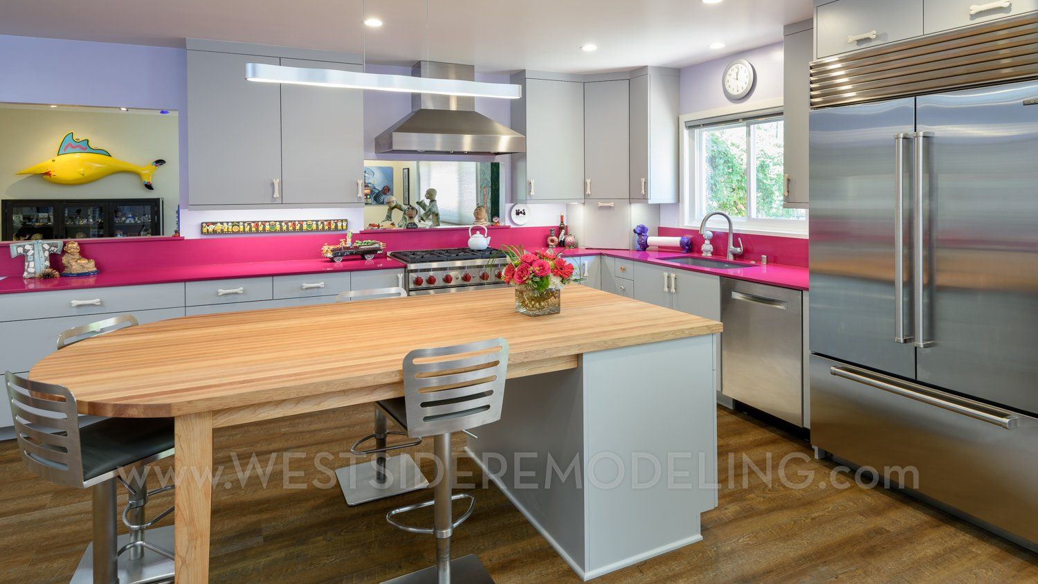 Modern kitchen with pink countertops, large island, stainless steel fridge, and hardwood floors