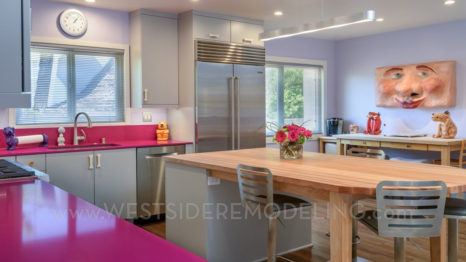 Modern kitchen with bright pink countertops, stainless steel appliances, and a dining table by a window.