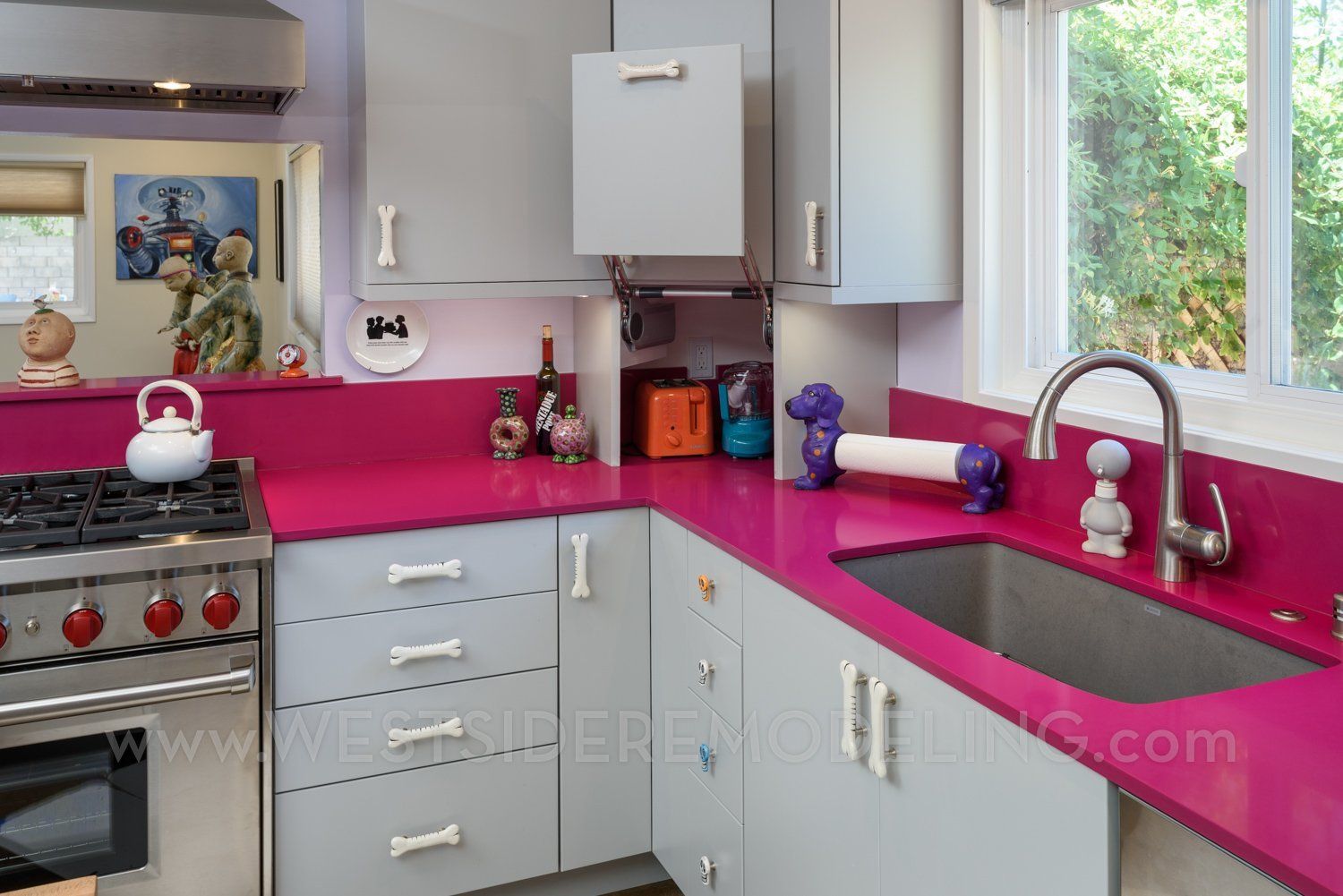 Bright kitchen with magenta countertops, gray cabinets, stove, sink, and a window view.