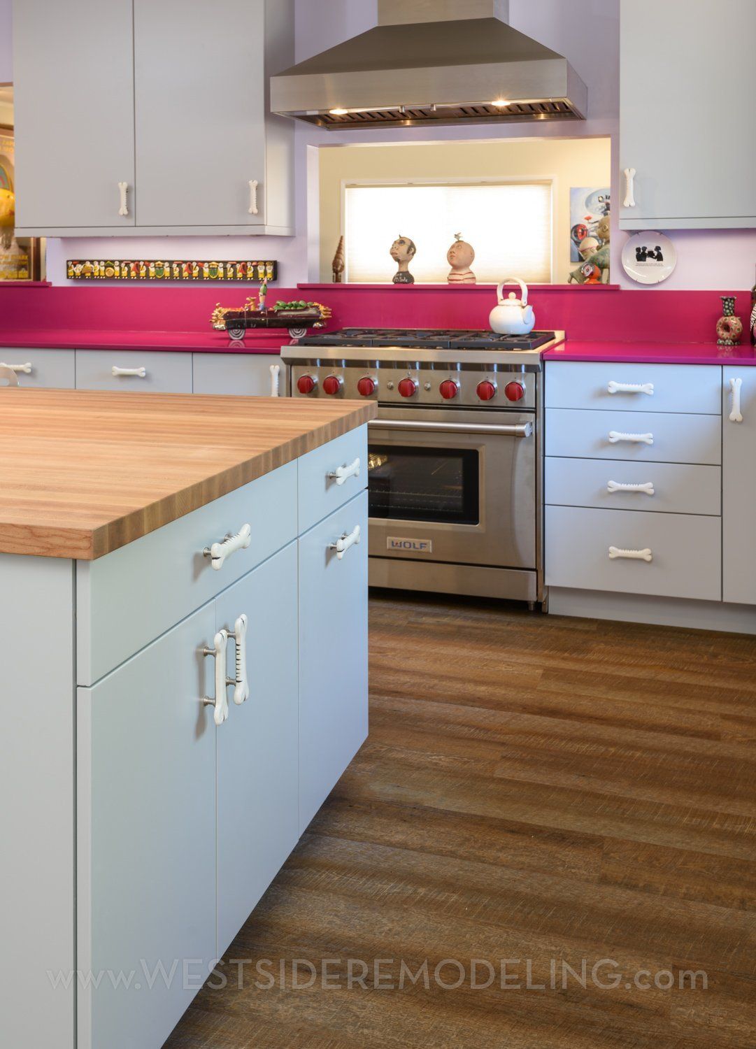 Modern kitchen with light blue cabinets, wood island, stainless steel stove, and magenta backsplash