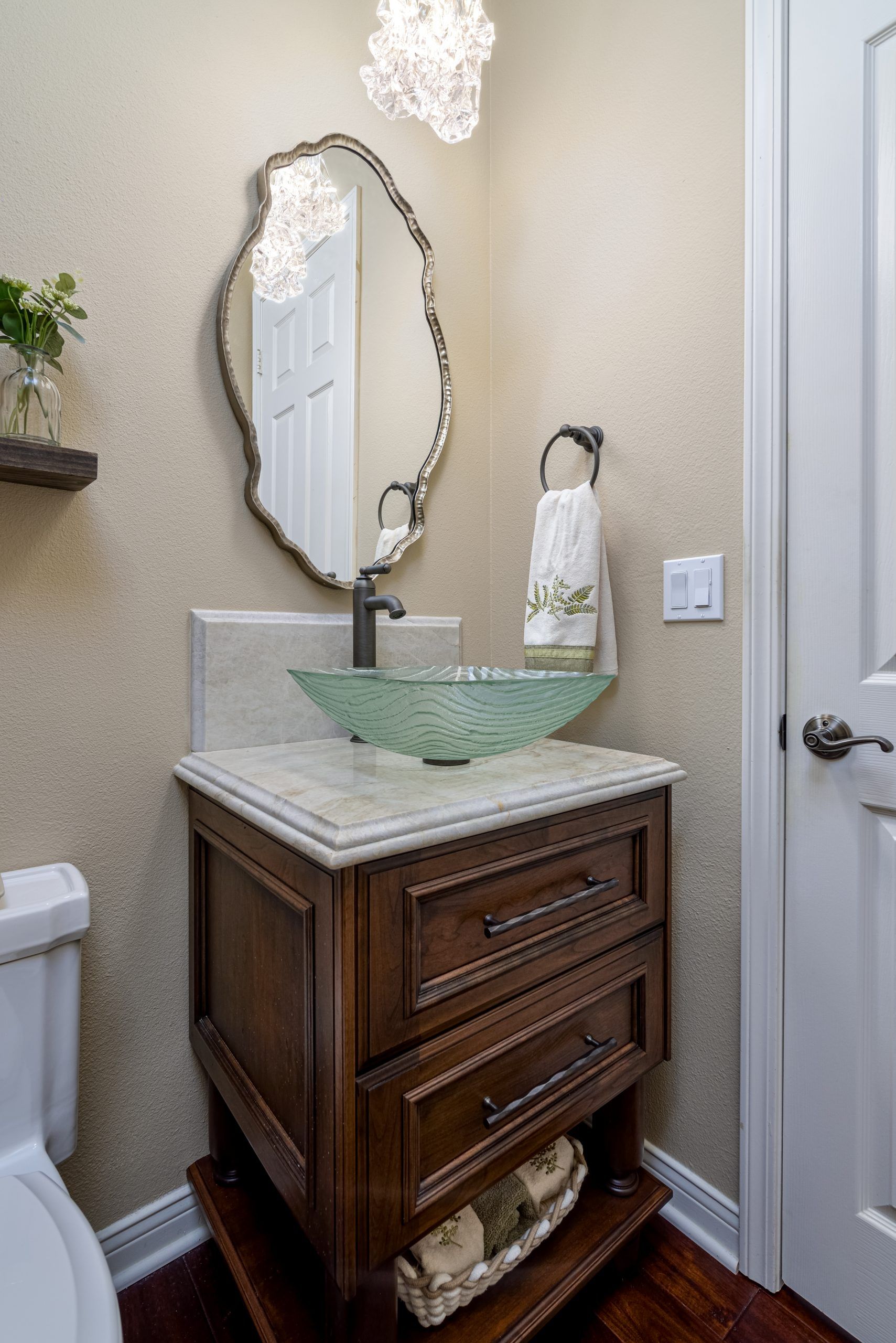 Small bathroom vanity with green glass sink, ornate mirror, towel ring, and white door.