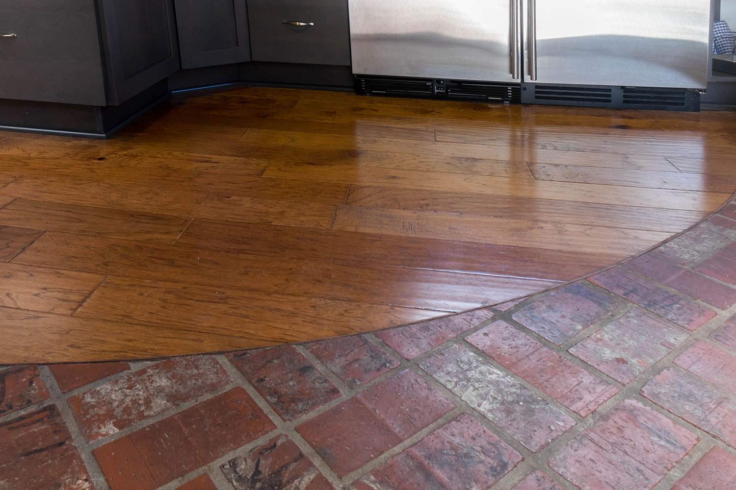 Kitchen floor with hardwood and brick tile transition in warm brown tones