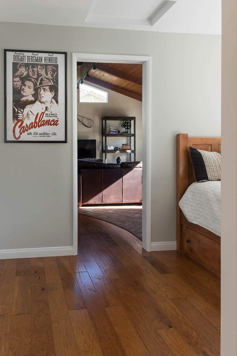 Bedroom with hardwood floors, white walls, framed art, and doorway to a bathroom with a vanity.