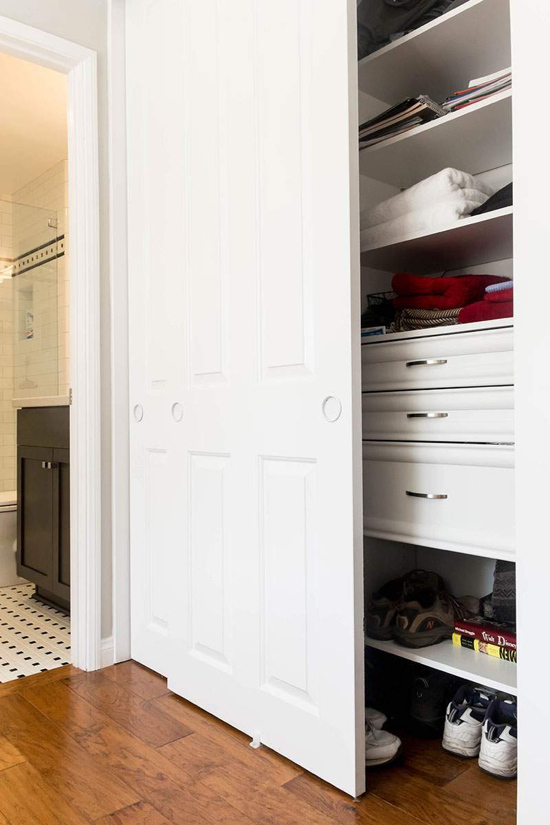 Open closet with shelves of folded clothes, drawers, and shoes beside a hallway.