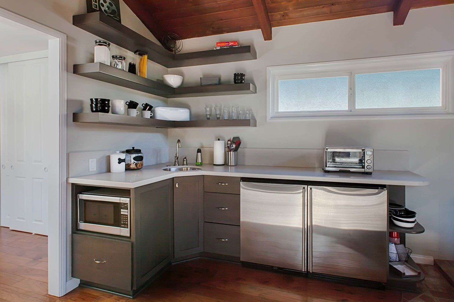Modern kitchen with open shelves, stainless steel dishwasher, countertop appliances, and a small window