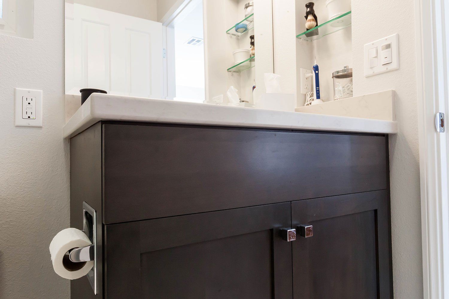 Dark bathroom vanity with white countertop and sink beside a toilet paper holder.
