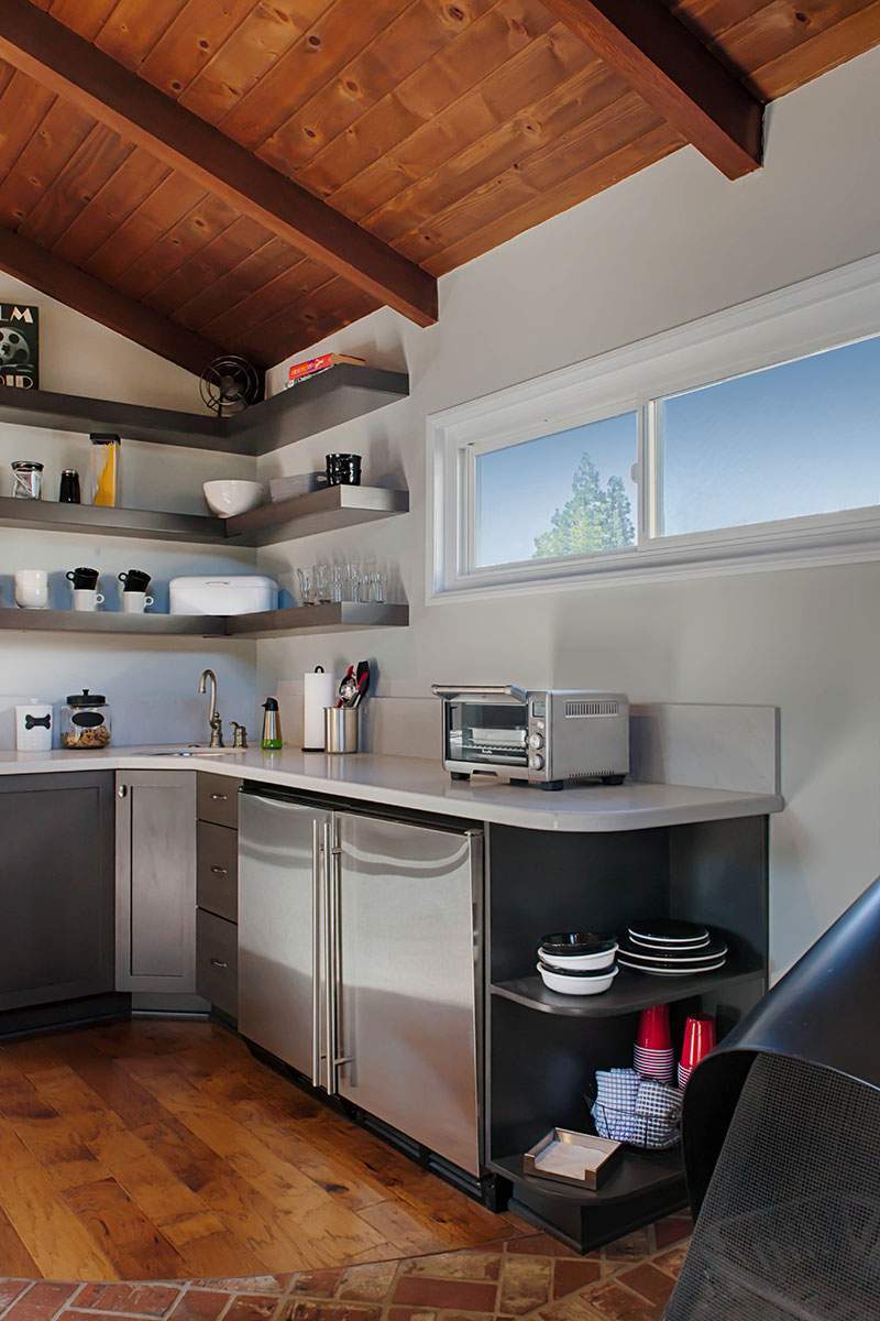 Modern kitchen corner with wood ceiling, open shelves, stainless appliances, and a window.