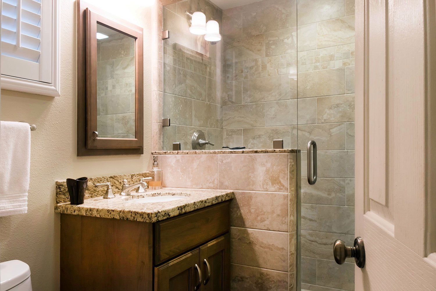 Modern bathroom with glass shower, stone vanity, mirror, and beige tile walls.