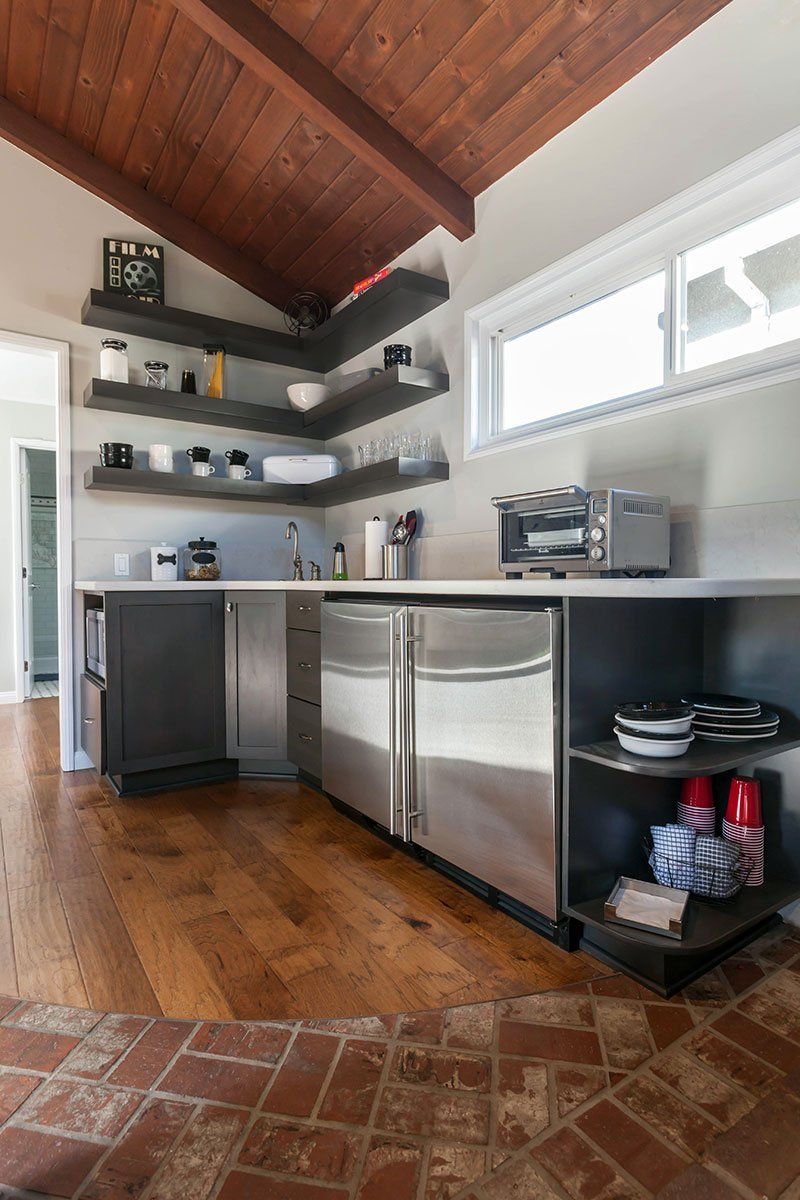 Modern kitchen with wood ceiling, stainless appliances, floating shelves, and window light