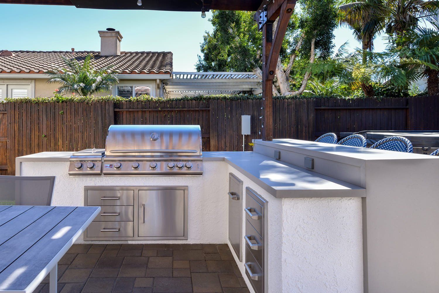 Outdoor kitchen with stainless steel grill, white counters, and a wooden fence in a backyard
