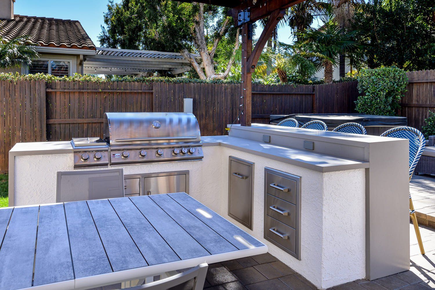 Outdoor patio with built-in grill, countertop, sink, and hot tub beside a wooden fence
