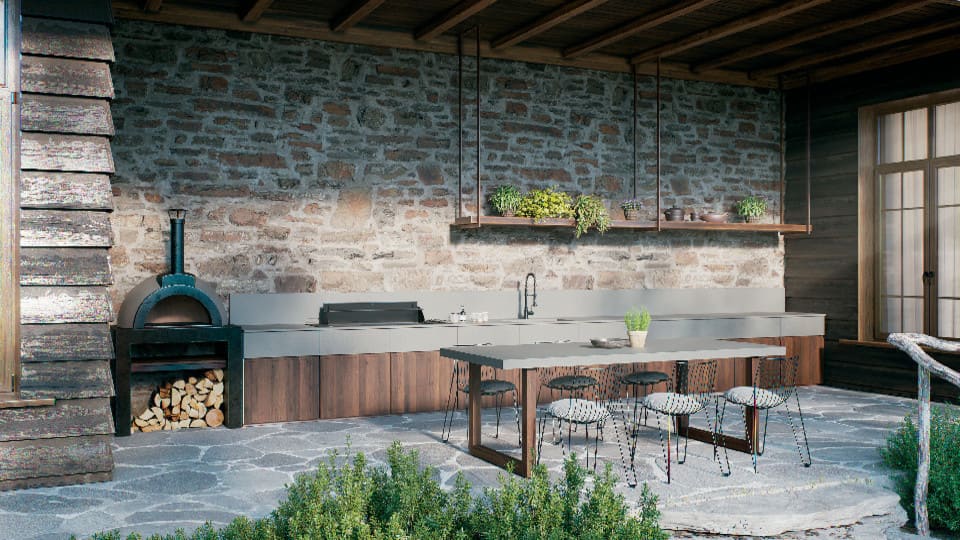 Rustic outdoor kitchen with stone wall, wood-fired oven, sink, countertop, and table under a roofed patio