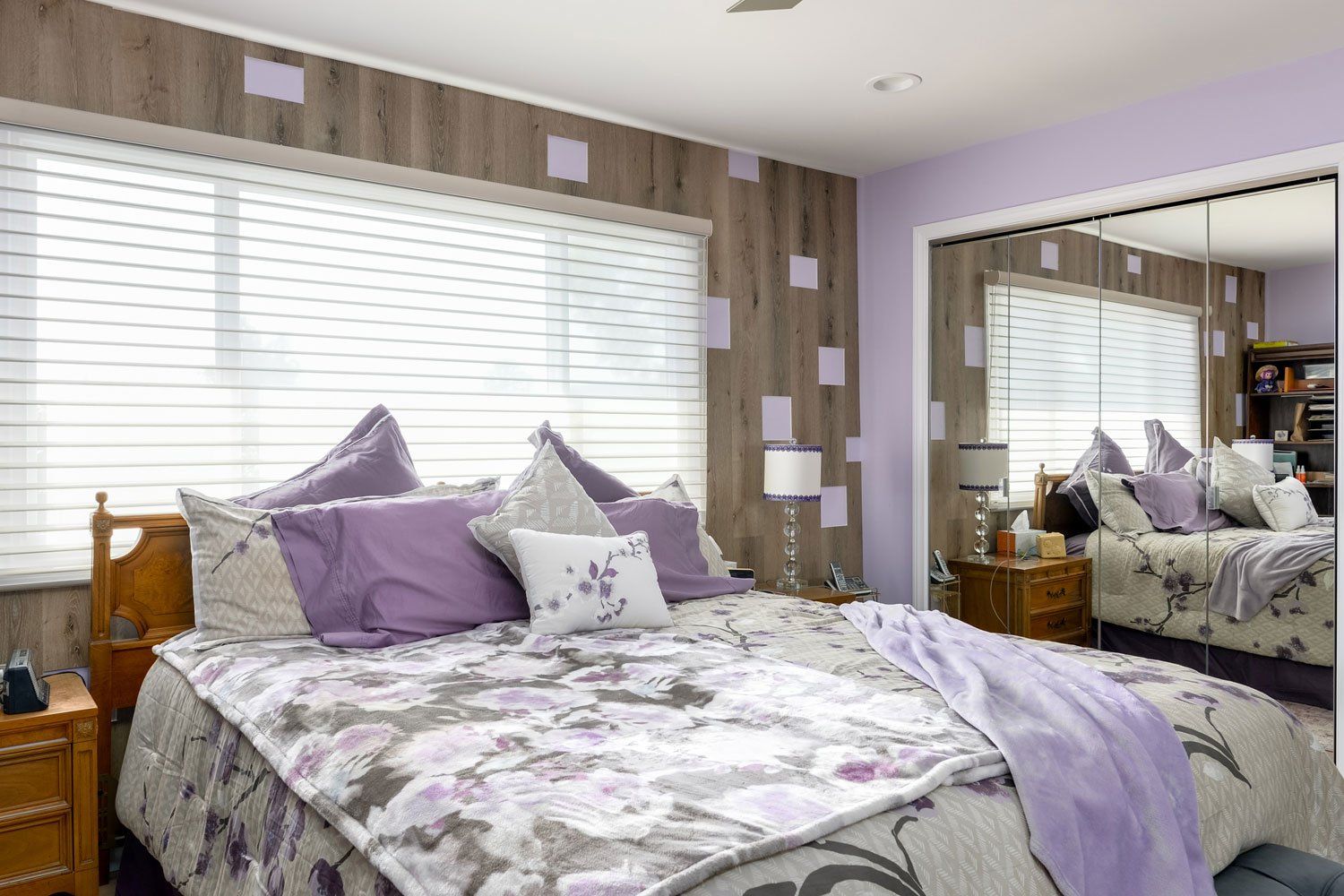 Bedroom with purple bedding, large window blinds, and mirrored closet doors reflecting the room