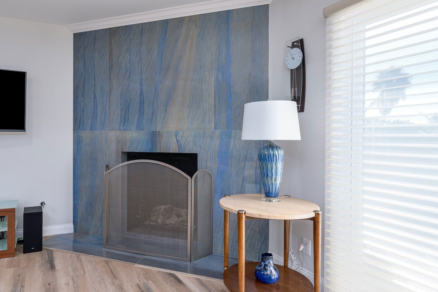 Living room with fireplace, blue accent wall, lamp on round table, and bright window blinds