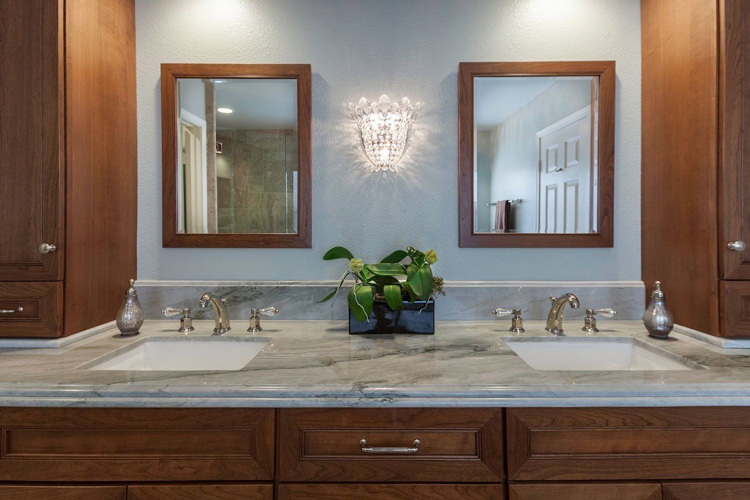 Bathroom vanity with double sinks, mirrors, wood cabinets, and a potted plant centerpiece