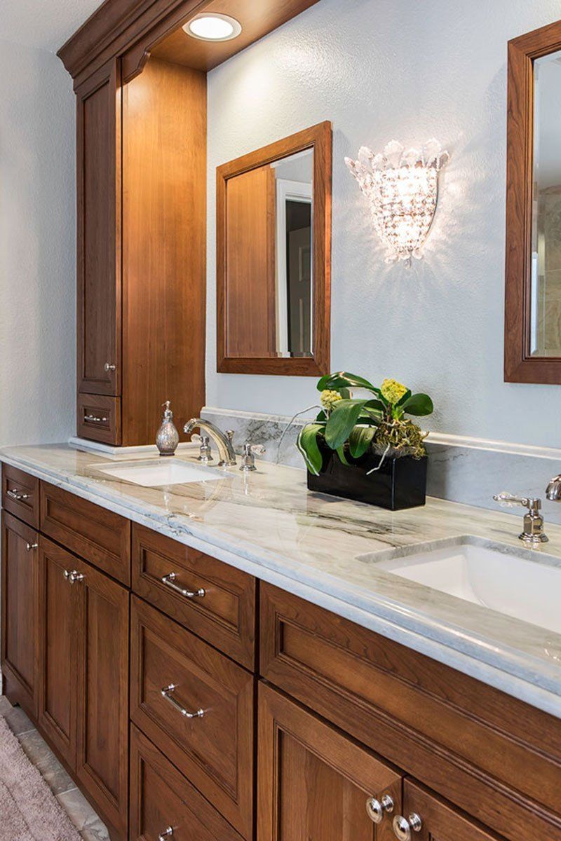 Elegant bathroom vanity with wood cabinets, marble countertop, mirrors, and wall sconces