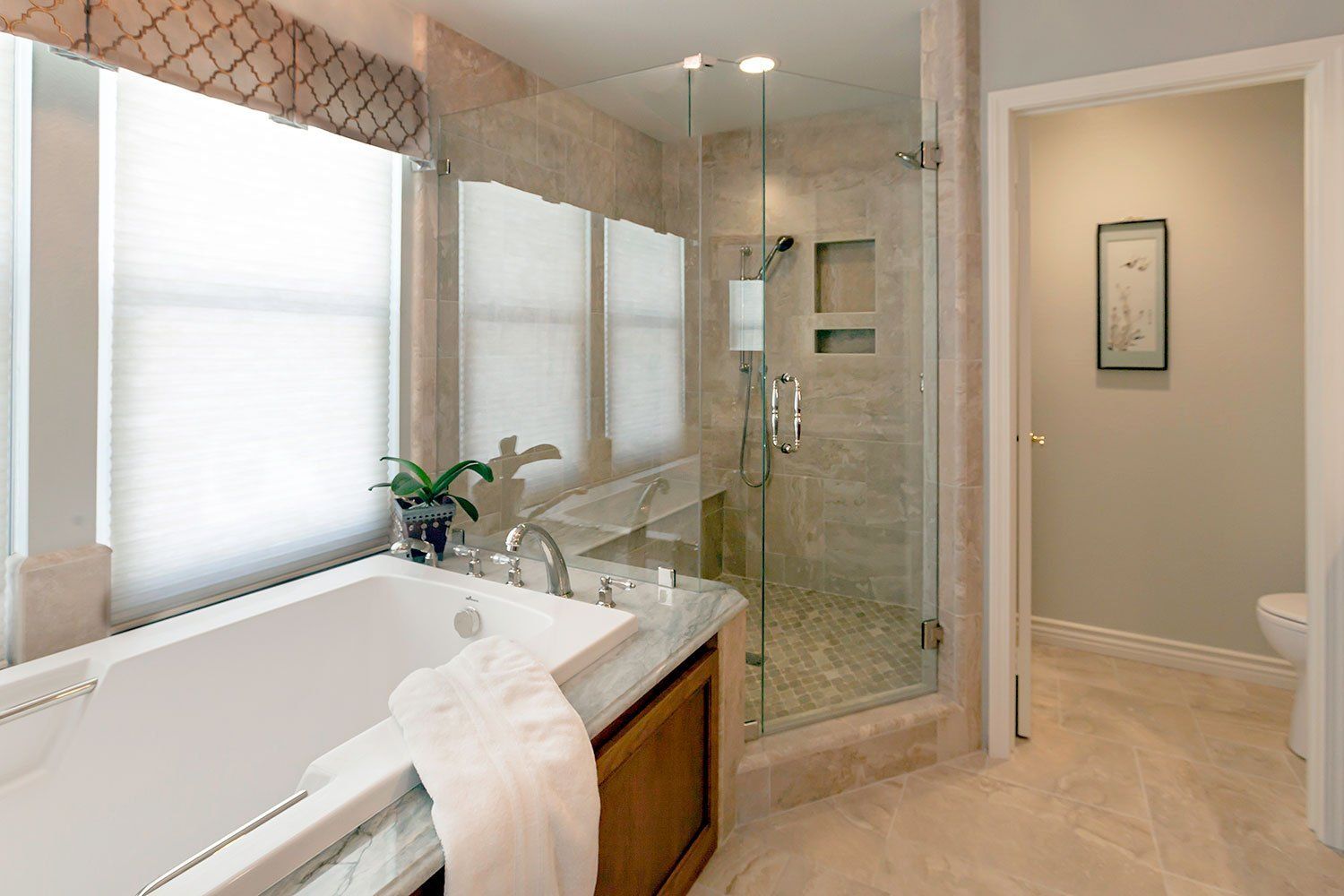 Bright bathroom with a soaking tub, glass shower, vanity, and beige tile walls and floor.