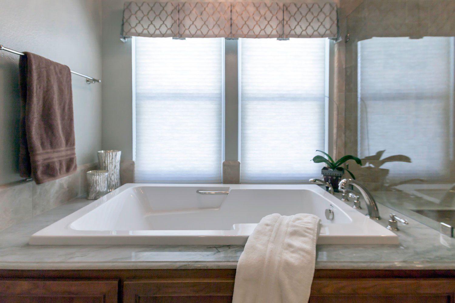 Bright bathroom with a soaking tub beneath three frosted windows and a towel draped over the edge