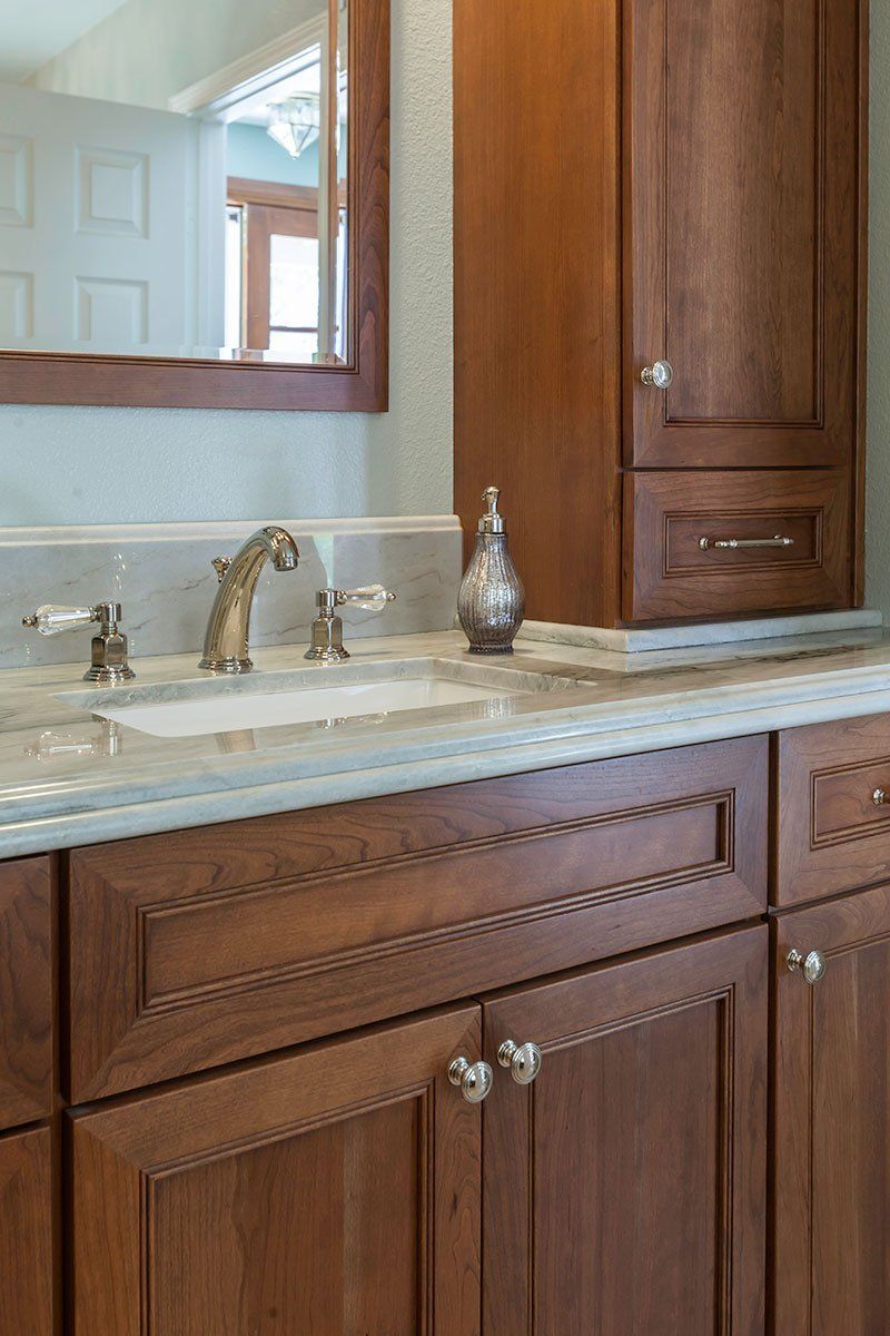 Wooden bathroom vanity with marble countertop, sink, and mirror against a light blue wall.