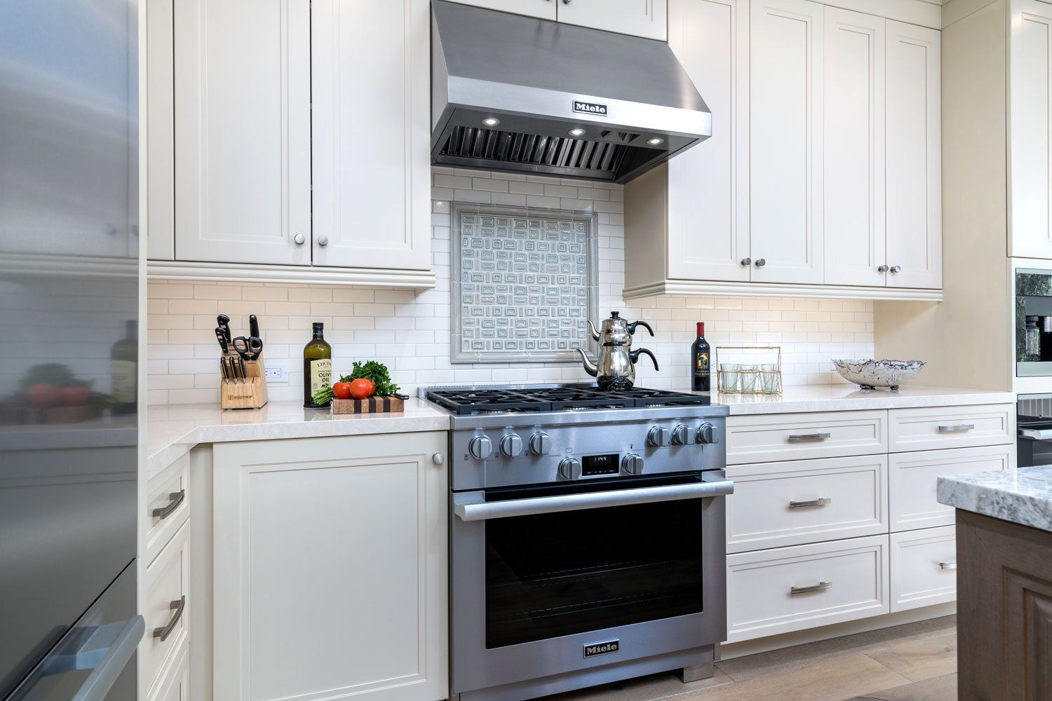 Bright modern kitchen with white cabinets, stainless steel stove, and marble countertops