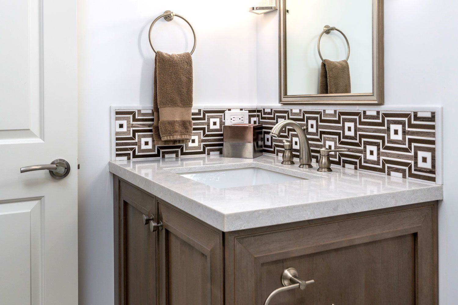 Bathroom vanity with white countertop, mosaic tile backsplash, and towel ring beside a mirror