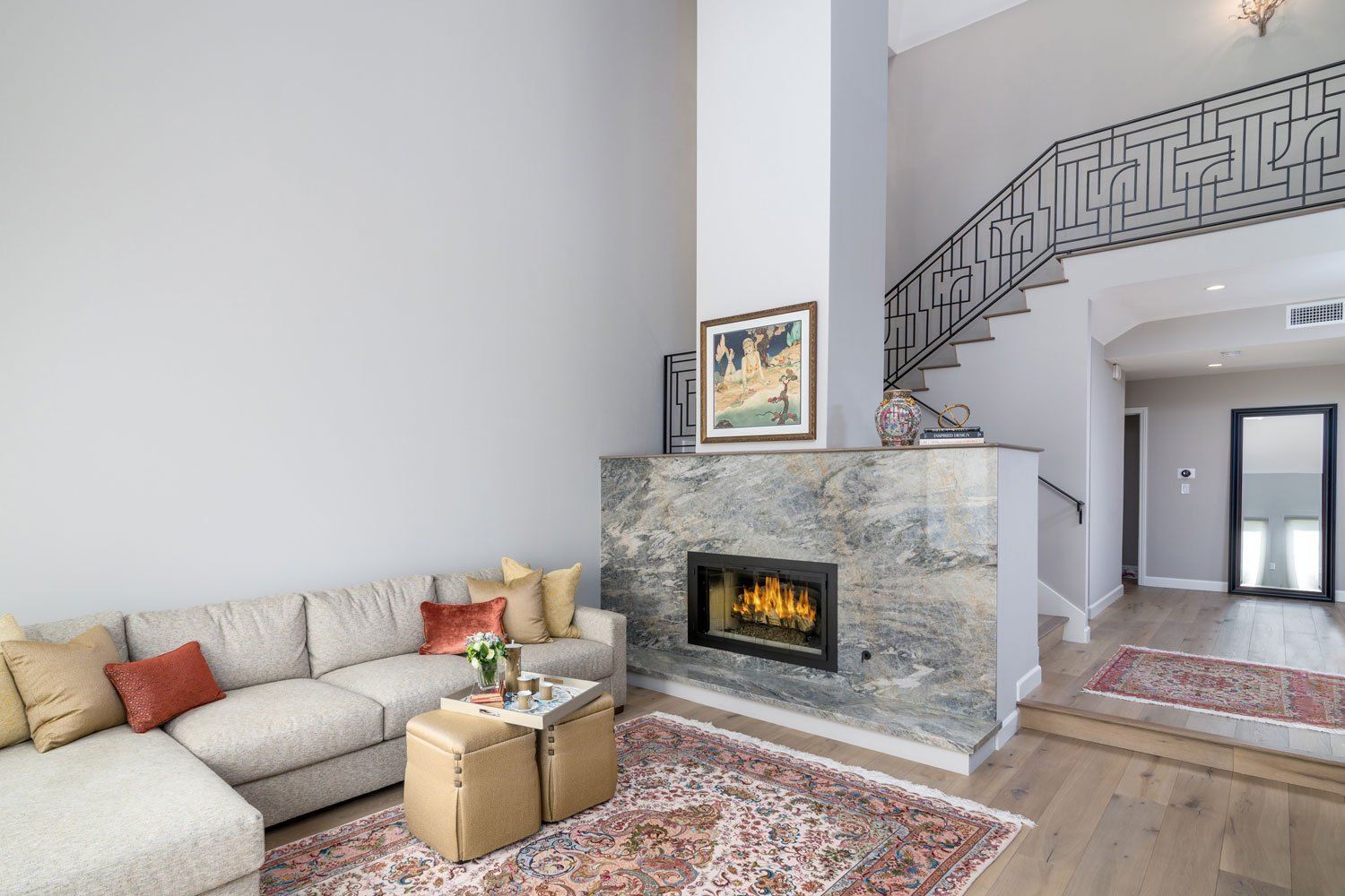 Bright living room with beige sectional, stone fireplace, staircase, and patterned rugs