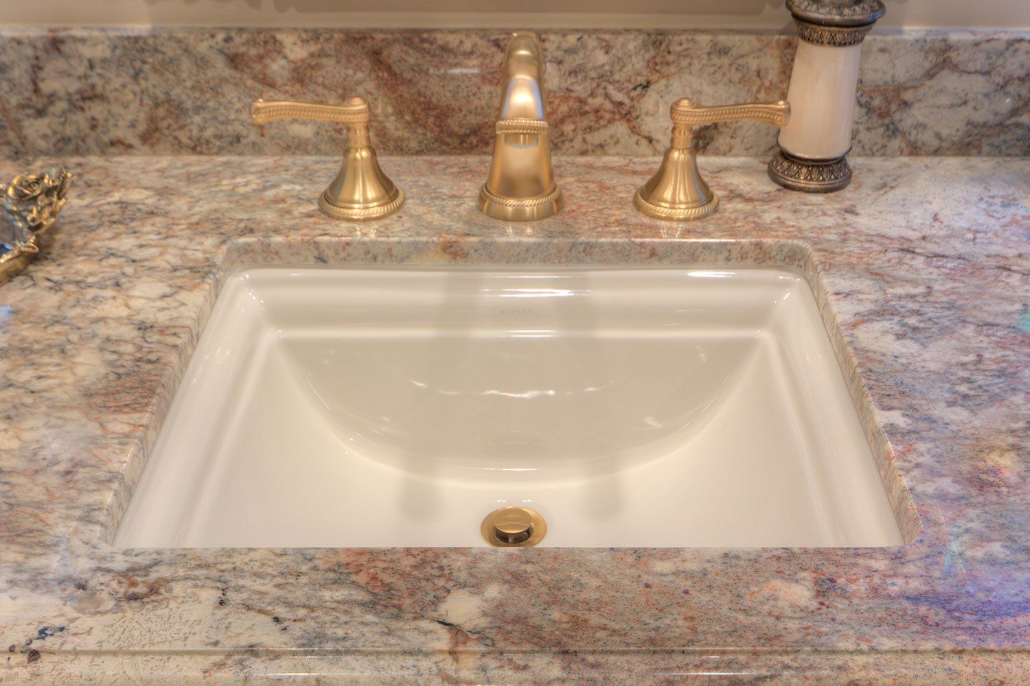 White bathroom sink with gold faucet on speckled stone countertop