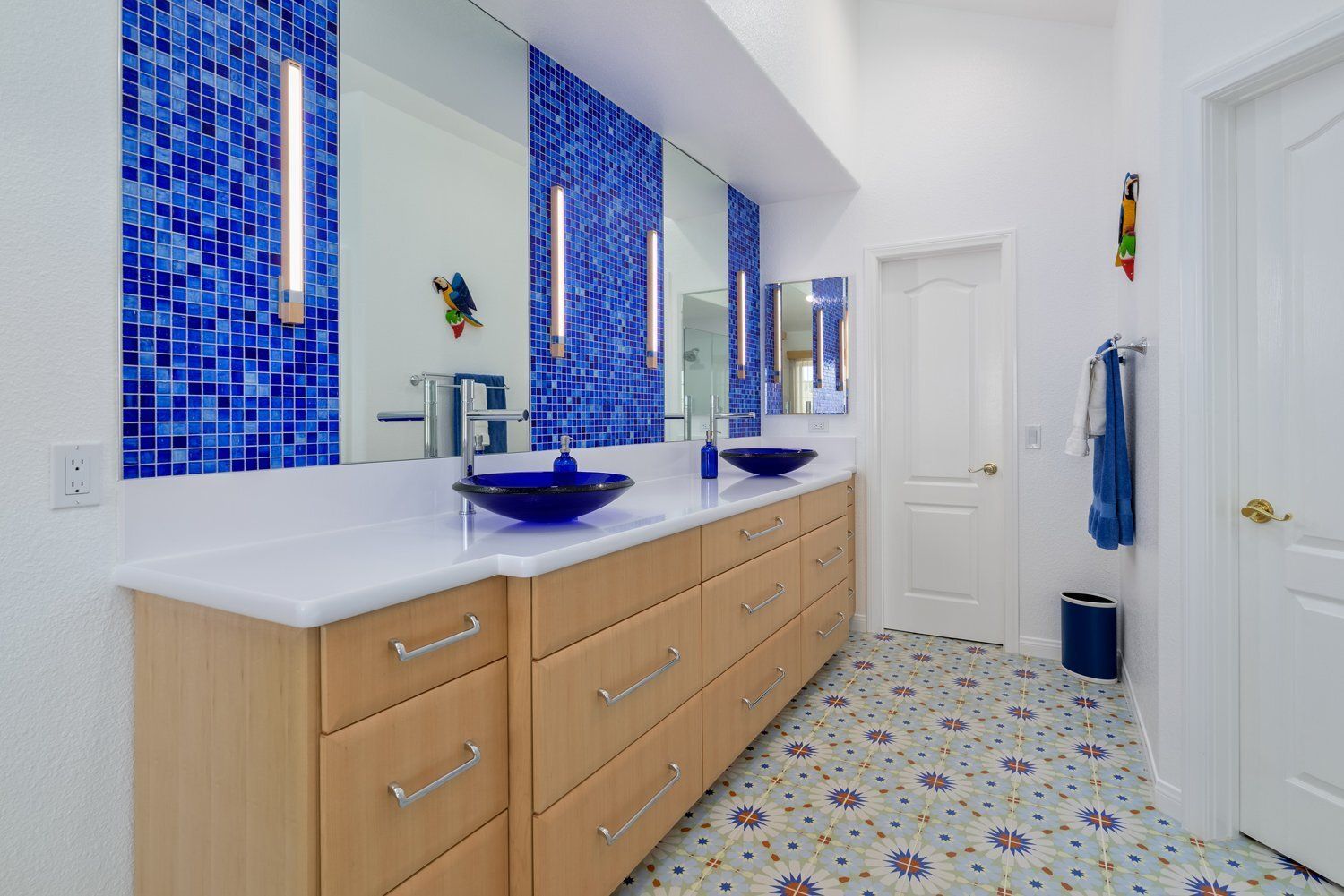 Bright bathroom with blue mosaic tile accents, double vanity, and patterned floor tiles