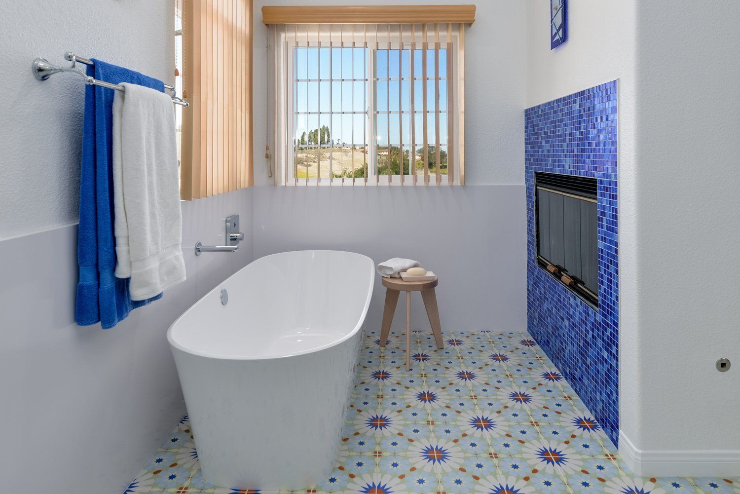 Bright bathroom with a freestanding tub, blue tile fireplace, patterned floor, and window blinds