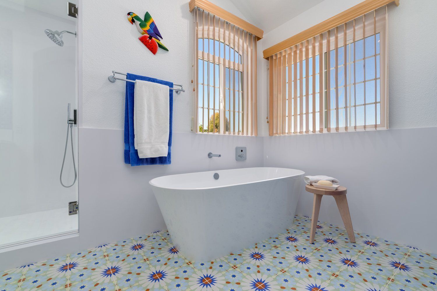 Bright bathroom with freestanding tub, blue towel, wooden stool, and colorful mosaic floor tiles