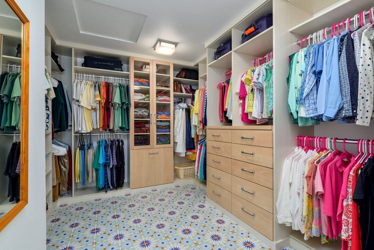 Walk-in closet with colorful clothes on shelves and racks, drawers, and a patterned floor.